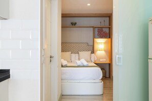 Une chambre d’hôtel avec un lit, une lampe de chevet et une petite étagère ornée d’objets décoratifs.