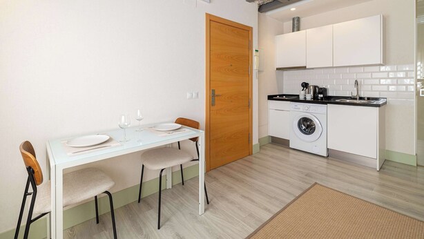 Una cocina funcional con lavadora, una mesa de comedor con sillas y una puerta de madera.