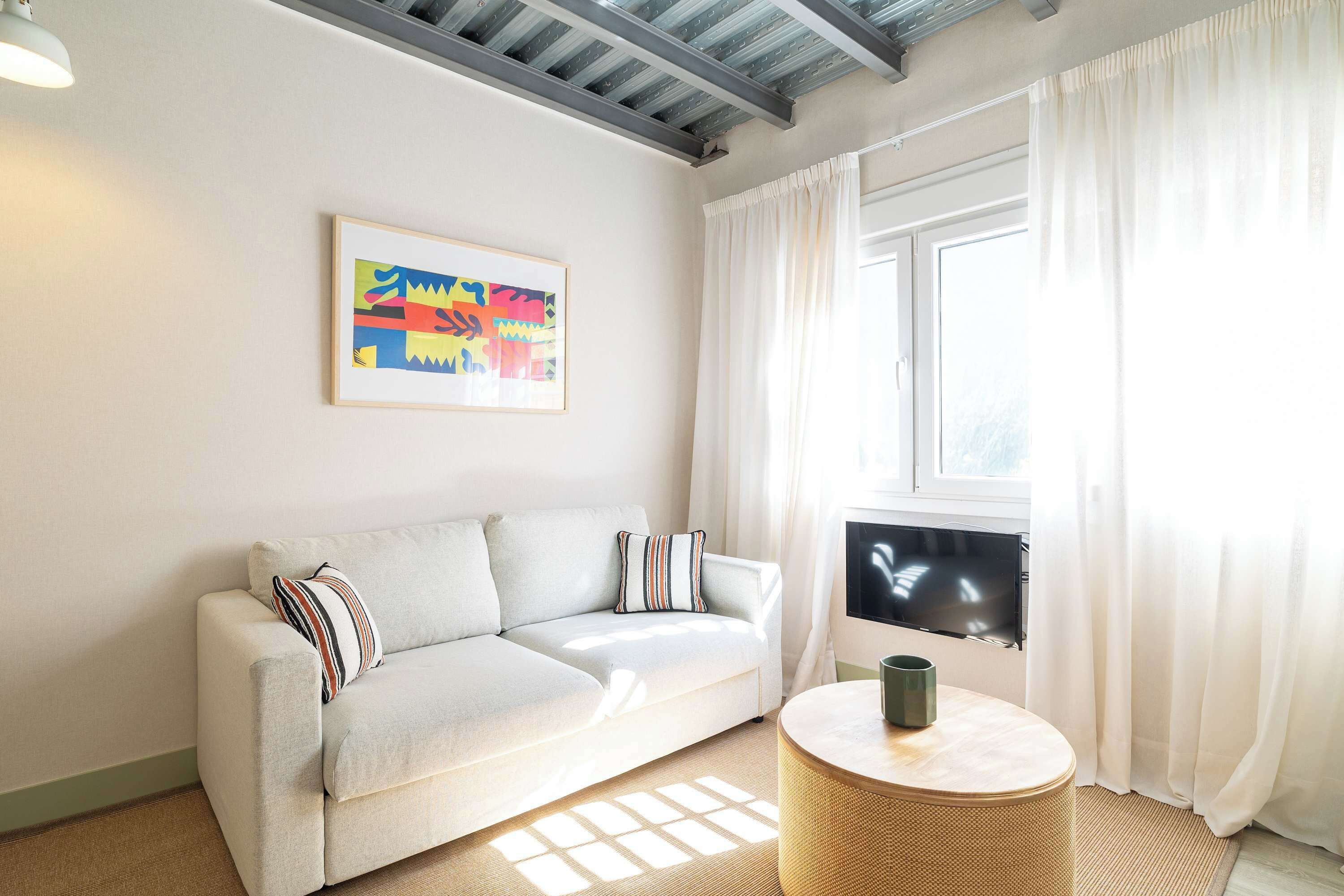 Una sala de estar moderna con un sofá, un cuadro abstracto enmarcado, un televisor y una mesita redonda.