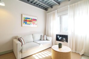 Ein modernes Wohnzimmer mit einer Couch, einem Bilderrahmen mit einem abstrakten Gemälde, einem Fernseher und einem runden Beistelltisch.