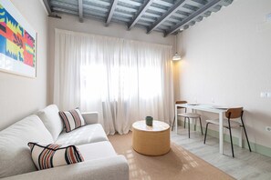 Un salon moderne comprenant un canapé, une table basse ronde, une table à manger avec des chaises et une grande fenêtre avec des rideaux.