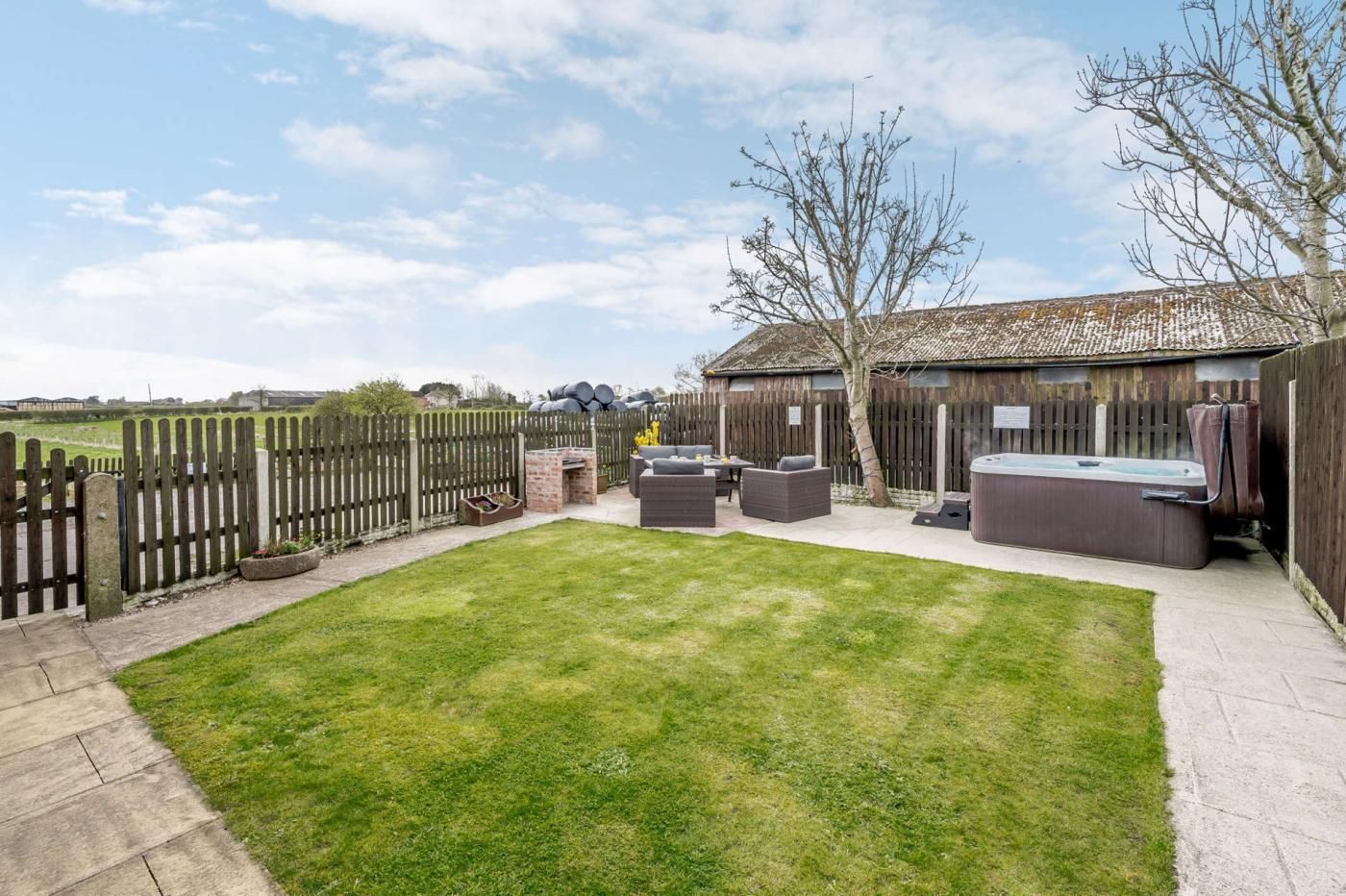A backyard with a grassy lawn, a wooden fence, a hot tub, and outdoor furniture.