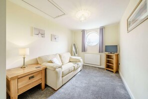 A small, cozy room with a sofa, a wooden side table, a television, and a radiator. - 3 Bed in Poulton-le-fylde (oc-41764) (Stalmine)
