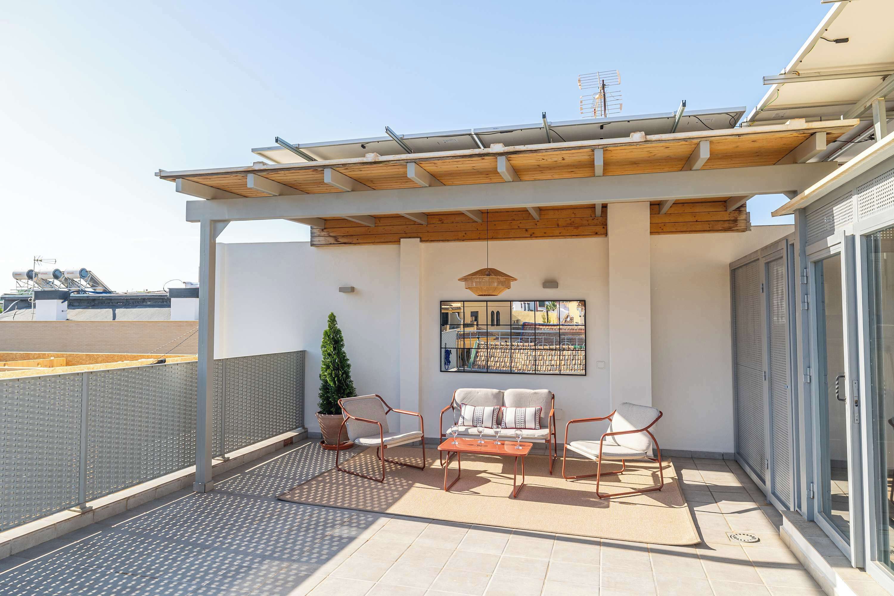 A covered outdoor seating area with a sofa, two chairs, and a table, a potted plant, and a view of the cityscape.