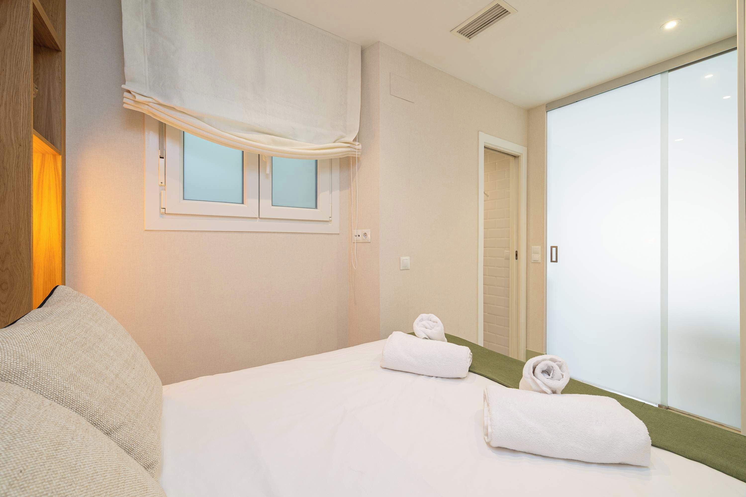 Una habitación de hotel con una cama, un ventanal con persiana blanca, una puerta y una pared verde.