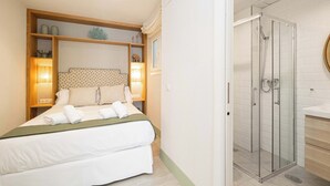 Hotellihuone, jossa on sänky, lasiseinällinen suihku ja puinen pääty, jossa on hyllyt.