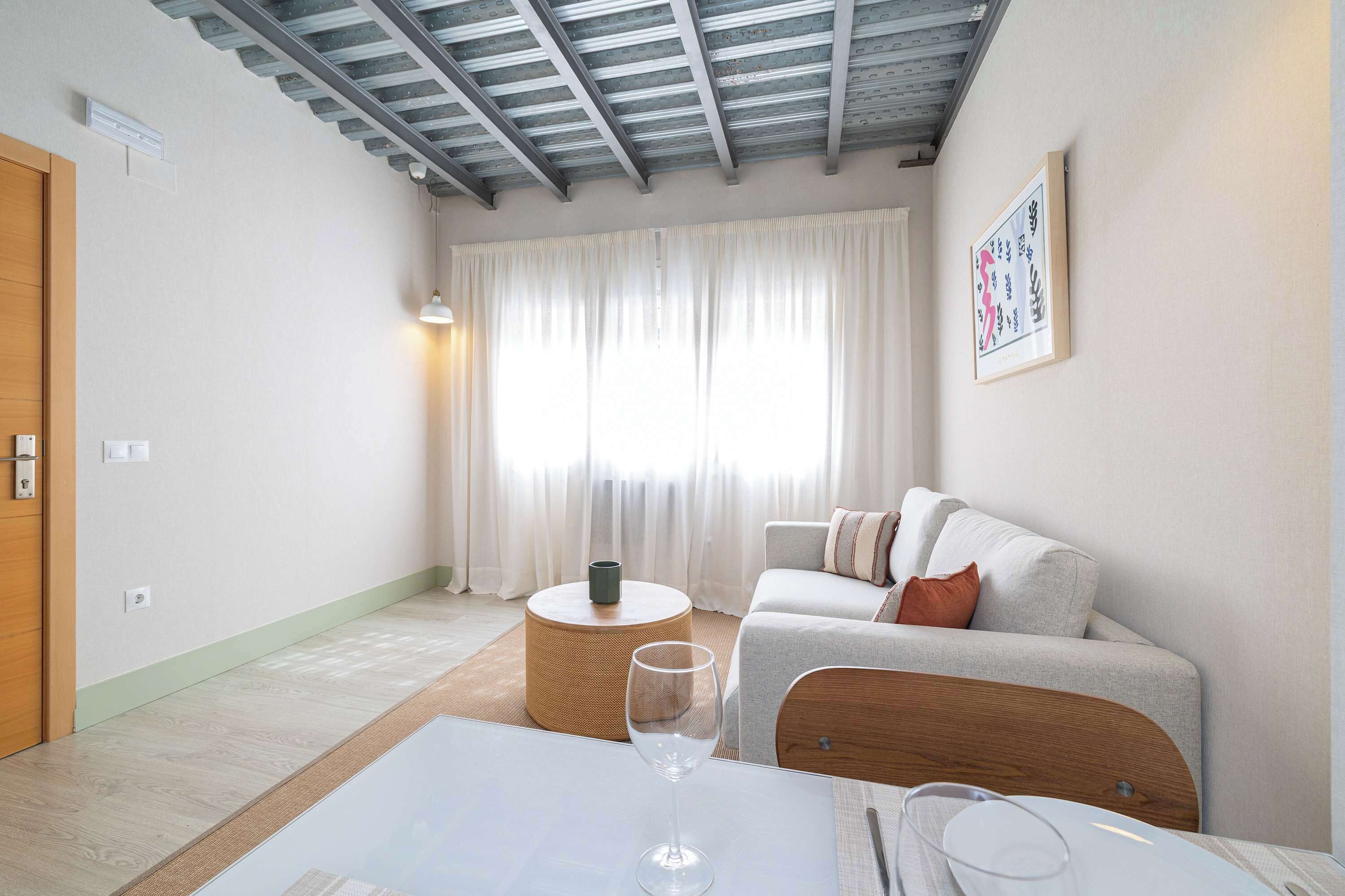 A modern living room with a sofa, a round coffee table, and a glass table with a wine glass.