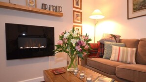 A living room with a fireplace, a sofa, a coffee table with books and candles, and a vase with flowers. - 2 Bed in Wells (oc-41654) (Wells)