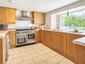 A modern kitchen with wooden cabinets, a gas stove, an oven, and a window with a view of greenery. - 4 Bed in Lampeter (oc-41577) (Cellan)
