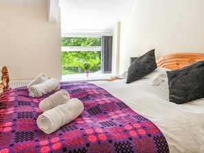 A hotel room with a bed, pillows, a window with a view of greenery, and a rolled towel on the bed. - 4 Bed in Lampeter (oc-41577) (Cellan)