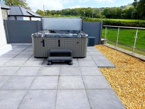 An outdoor hot tub with a bench in front, surrounded by a paved patio and a gravel area. - 4 Bed in Lampeter (oc-41577) (Cellan)
