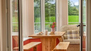 A cozy seating area with a wooden table, benches, and a wicker chair, overlooking a green landscape. - 4 Bed in Lampeter (oc-41577) (Cellan)