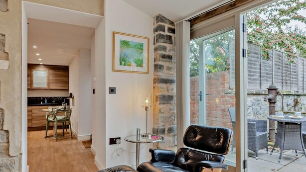 Een modern interieur met een lederen fauteuil, een eetgedeelte, een keuken en een grote glazen deur die uitkomt op een terras.