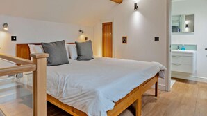 Een slaapkamer met een houten bed, witte beddengoed, een houten hoofdbord, een houten plafondbalk en een klein nachtkastje.