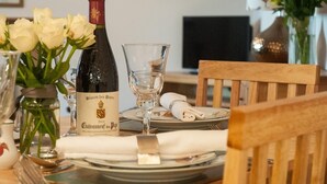 A dining table set with a bottle of Blason des Papes wine, a glass, and a vase with white flowers. - 2 Bed in Launceston (oc-41992) (Saint Giles on the Heath)