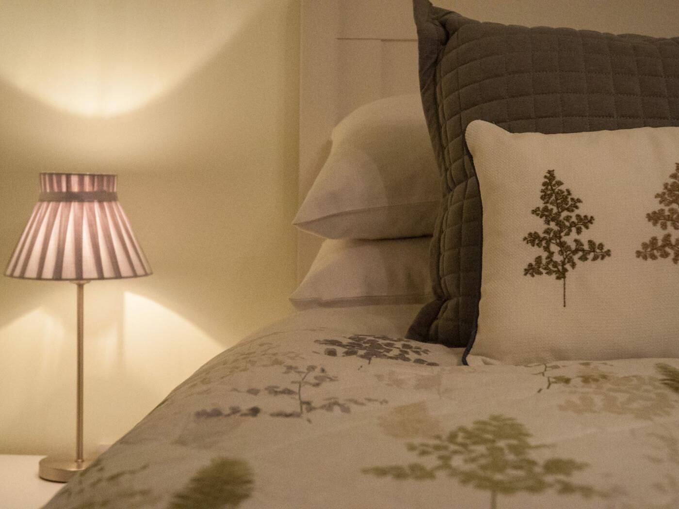 Uma cama com um edredom estampado com flores, um abajur e uma parede com acabamento texturizado.