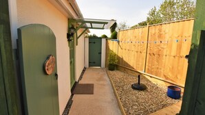 A narrow pathway leading to a wooden gate, a small garden area with gravel and a wooden deck, and a green fence. - 1 Bed in Par- (oc-42007) (Par)