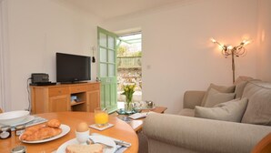 A cozy living room with a television, a dining table set with breakfast, a sofa, and a decorative light fixture. - 1 Bed in Par- (oc-42007) (Par)