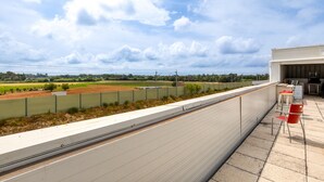 A rooftop terrace with a view of a green field and a body of water.