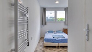 A bedroom with a bed, a radiator, a window, and a door.