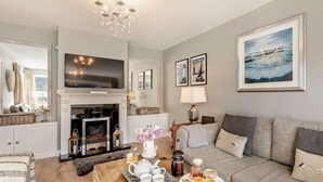 A living room with a fireplace, a sofa, a coffee table with breakfast items, and a television. - 3 Bed in Ilfracombe (oc-41580) (Combe Martin)