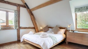 A bedroom with a sloped ceiling, wooden beams, a bed with pillows, a bedside table with a lamp, and a window with curtains. - 3 Bed in Worcester (oc-41983) (Little Green)