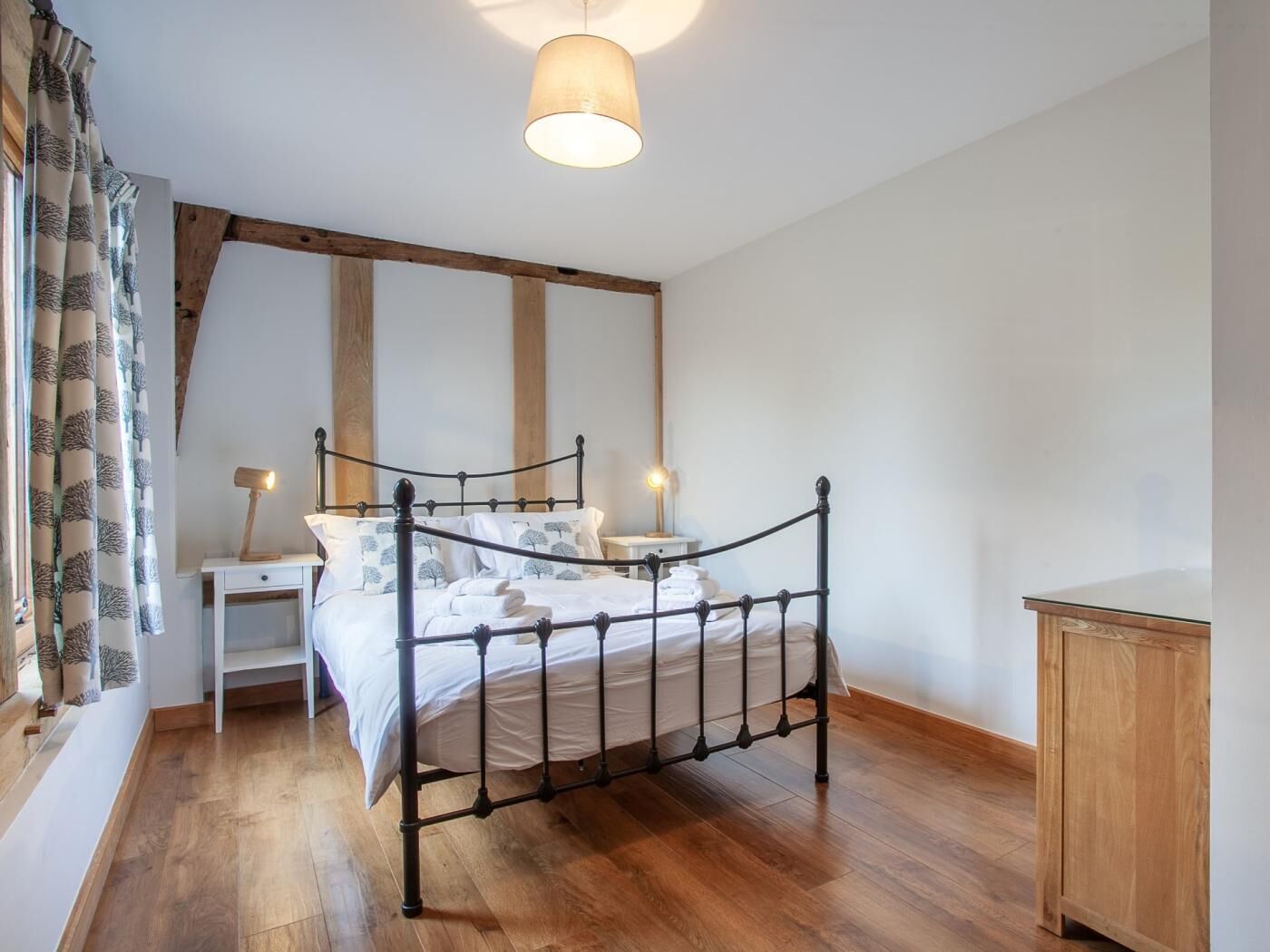 Un dormitorio con estructura de cama de metal, ropa de cama blanca, un armario de madera y una lámpara colgante.