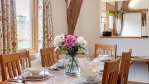 A dining area with a wooden table set for four, a vase of flowers, and a large window with curtains. - 3 Bed in Worcester (oc-41983) (Little Green)