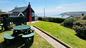 Une propriété située en bord de mer, dotée d’une pelouse verdoyante, d’une table de pique-nique et offrant une vue sur la mer.