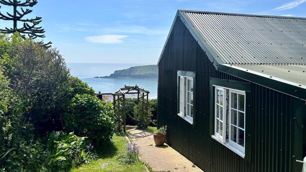 Un bâtiment situé sur la côte, doté d’un toit en métal, d’un jardin agrémenté d’une pergola en bois et offrant une vue sur la mer.