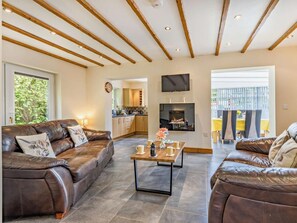 A living room with leather sofas, a coffee table, a fireplace, a TV, and a kitchen in the background. - 2 Bed in Tyn-y-gongl (oc-42369) (Marianglas)
