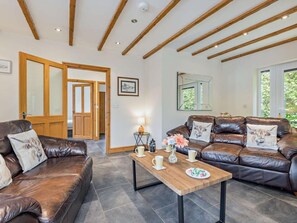 A spacious living room with a brown leather sofa, a wooden coffee table, and a large mirror on the wall. - 2 Bed in Tyn-y-gongl (oc-42369) (Marianglas)