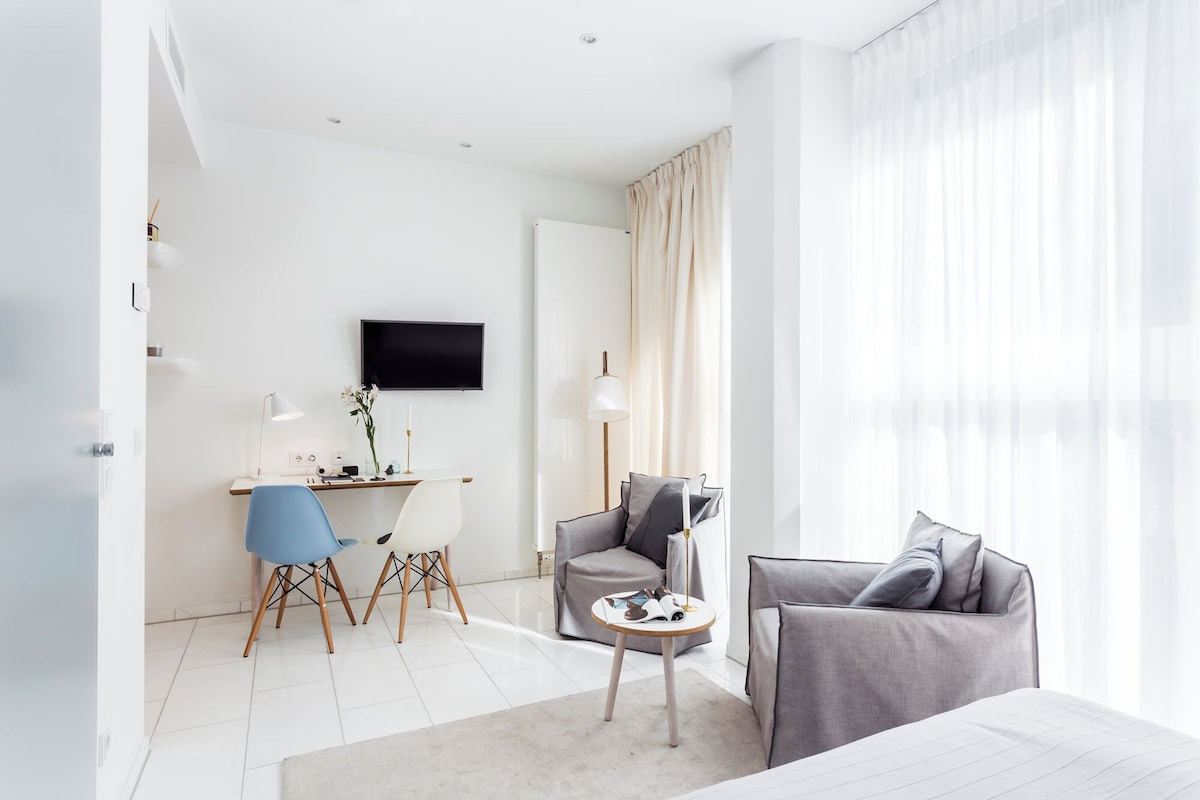 Ein modernes Hotelzimmer mit einem Bett, zwei Sesseln, einem Schreibtisch und einem Fernseher.