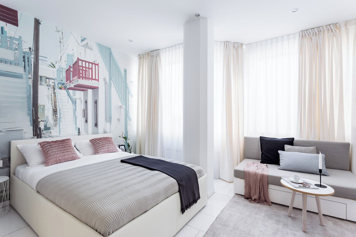 Ein modernes Schlafzimmer mit einem großen Bett, einer Couch, einem kleinen Tisch und einer Wand mit Stadtlandschaftsmalerei.