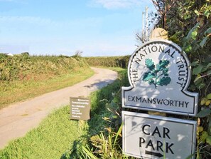 Ein Schild für den National Trust Parkplatz Exmansworthy mit einem kleinen Hinweisschild darunter.