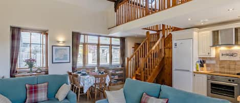 A spacious living area with two sofas, a dining table, and a kitchen with wooden beams and a staircase.