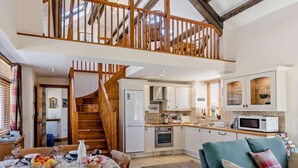 A spacious loft with a wooden staircase, a kitchen with white cabinets, and a dining area with a table set for four. - 3 Bed in Bideford (oc-42184) (Hartland)