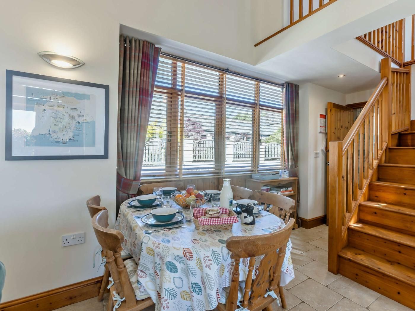 A dining area with a table set for four, a wooden staircase, and a map on the wall.