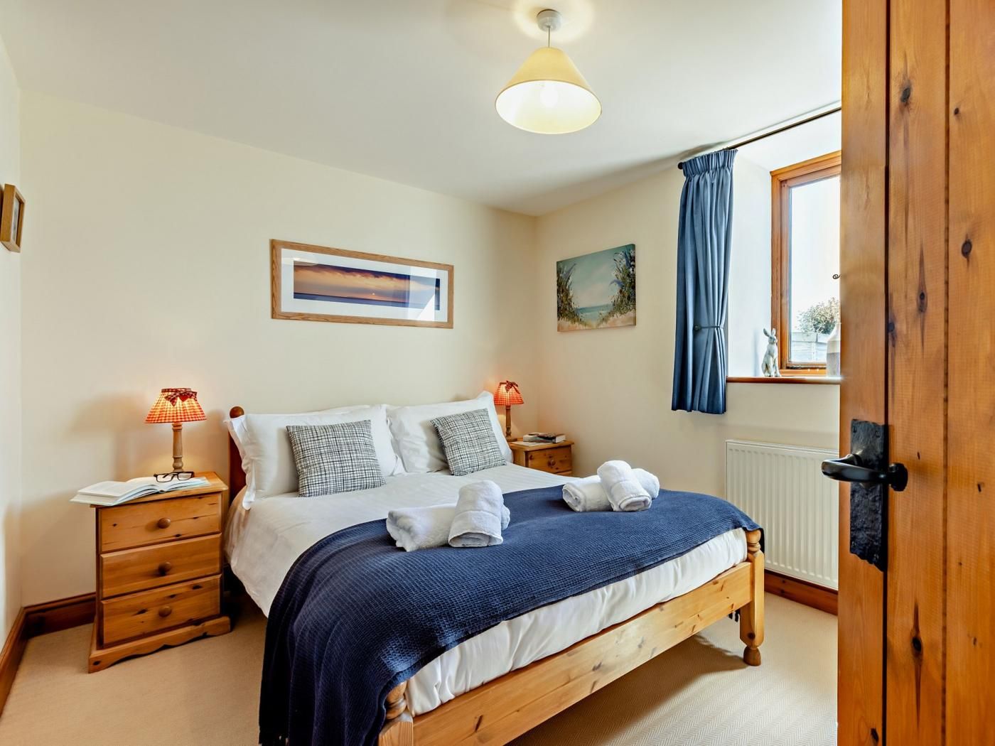 A bedroom with a bed, bedside tables, a window with curtains, and a door.