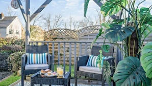 A patio with wicker furniture, a table with food and drinks, and large tropical plants. - 1 Bed in Bridgend (oc-42314) (Bryncethin)