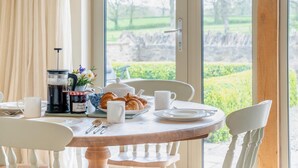 A breakfast table with croissants, coffee, and a view of a garden through a glass door. - 2 Bed in Sherborne (oc-41897) (Ryme Intrinseca)