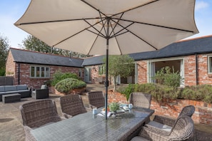 A patio with a table and chairs, a large umbrella, and a brick house with a garden. - 4 Bed in Dorchester (oc-42204) (Sydling Saint Nicholas)