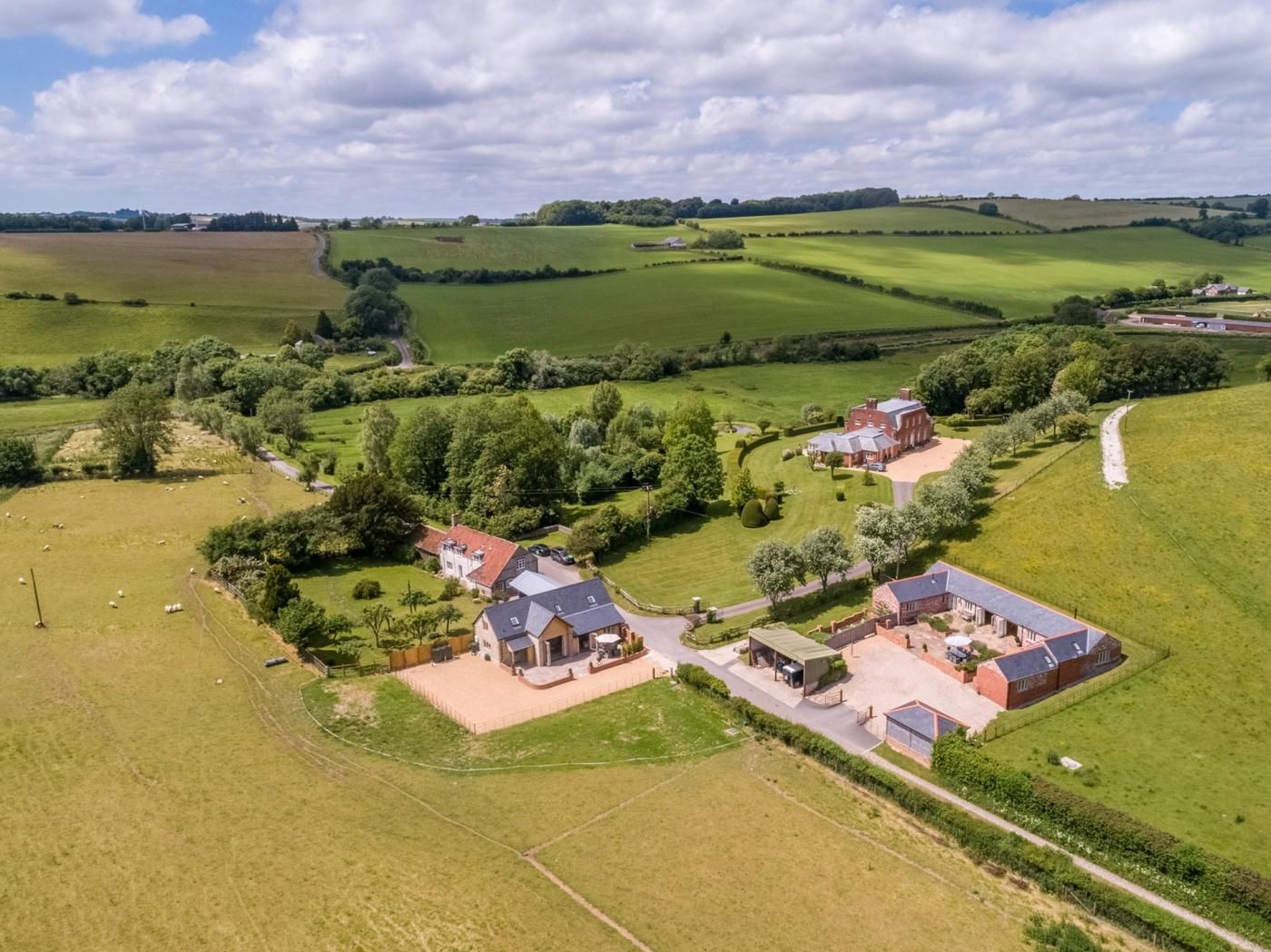 An aerial view of a rural property with multiple buildings, green fields, and a winding road.