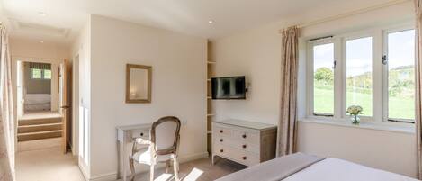 A bedroom with a bed, a desk, a chair, a television, and a window with a view of greenery.