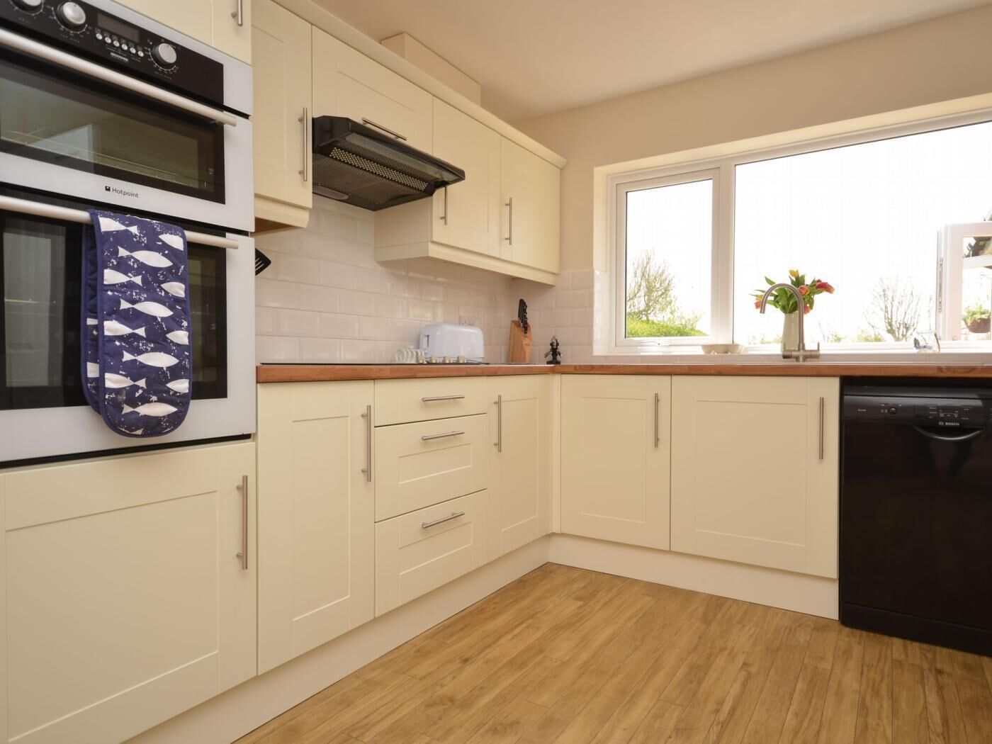 A kitchen with white cabinets, a Bosch dishwasher, a toaster, and a window with a view of greenery.