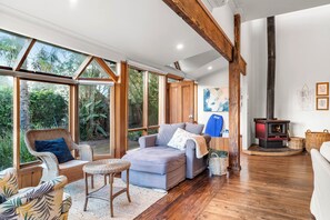 Ein gemütliches Zimmer mit großem Fenster, einer Couch, einem Sessel, Holzboden und Kamin.