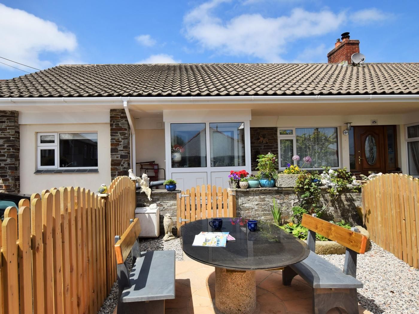 A house with a tiled roof, a front door, and a patio area with a table and benches.