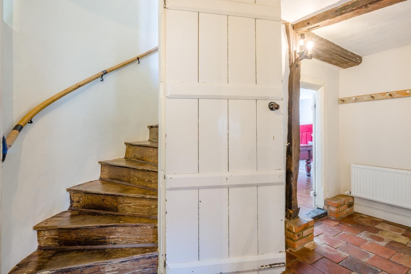 Un escalier en bois avec une porte blanche qui mène à une pièce dotée d’un radiateur et d’un plancher en briques.