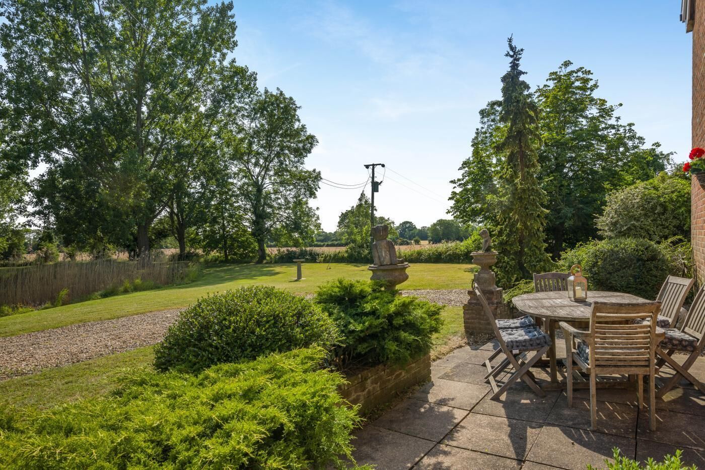 A patio with a table and chairs, surrounded by greenery and a view of the countryside.