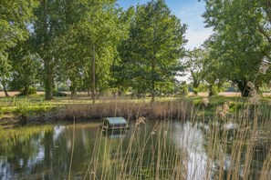 Un estany tranquil amb un petit moll, envoltat d'arbres verds i frondosos i una zona enjardinada.